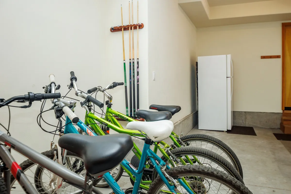 This image features bicycles stored in a garage area along with a refrigerator and utility supplies, suggesting an active lifestyle and readiness for family adventures. The mood is casual and energetic, hinting at easy access to biking and recreation.