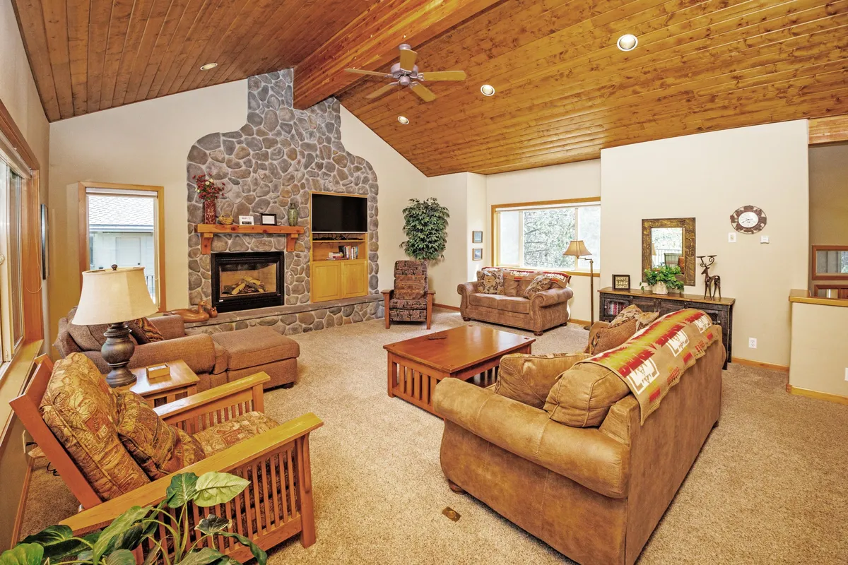 A warm, inviting interior living area with a stone fireplace, wooden ceiling, large windows, and ample comfortable seating. The space is ideal for relaxing, hosting friends, or enjoying game nights—all key activities described in the section.