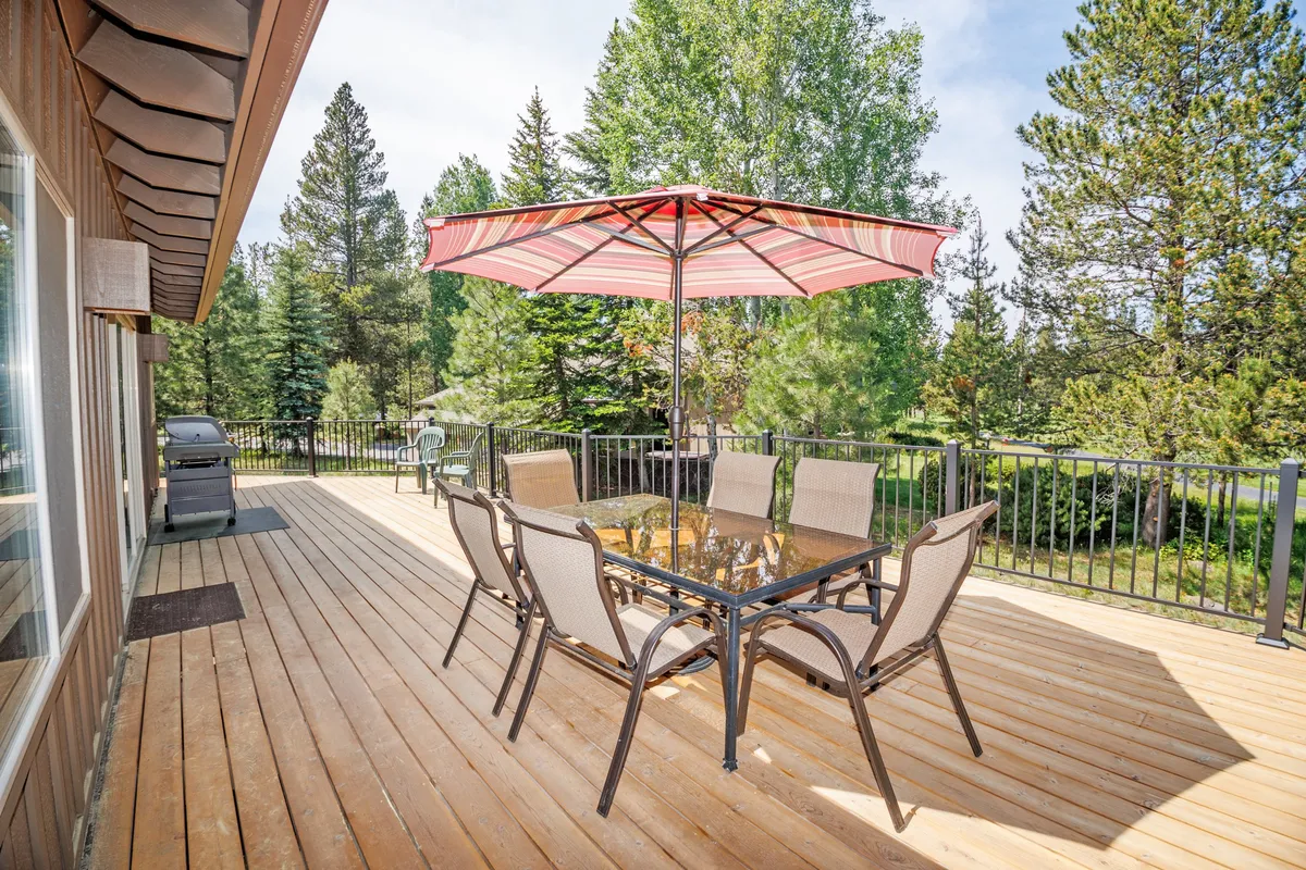 The photo features an outdoor dining table shaded by an umbrella, surrounded by towering trees. The scene feels social and relaxed, perfect for group meals, sunset dinners, or celebrations with friends in the fresh air.