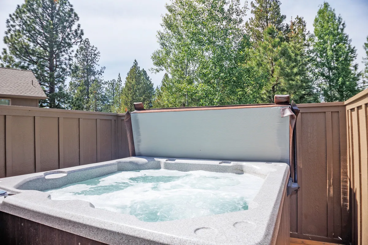 This image features a private hot tub nestled among tall trees, providing a sense of seclusion and natural beauty. The privacy fence and serene surroundings create an inviting atmosphere for relaxation, especially under the stars.