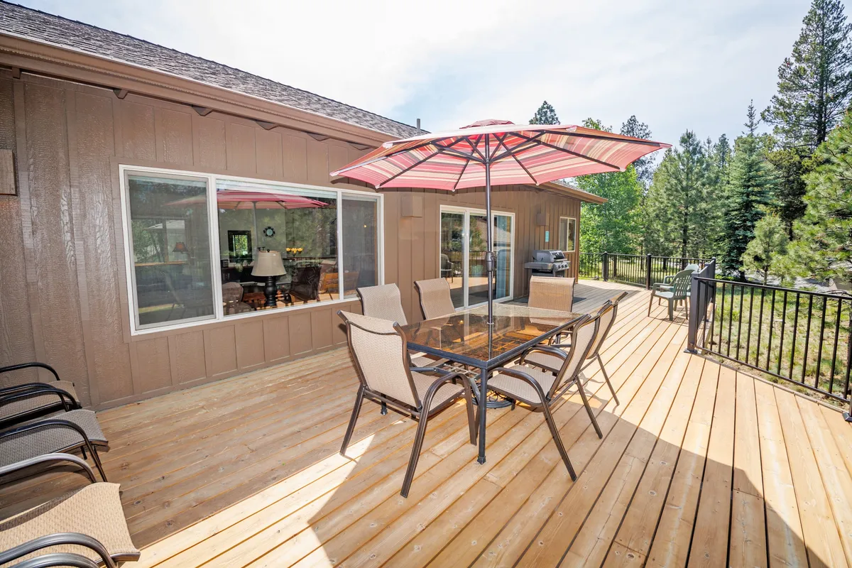 This exterior image features a glass dining table with a red and white striped umbrella, surrounded by greenery and comfortable chairs, suggesting an inviting space for outdoor dining, family gatherings, and relaxation.