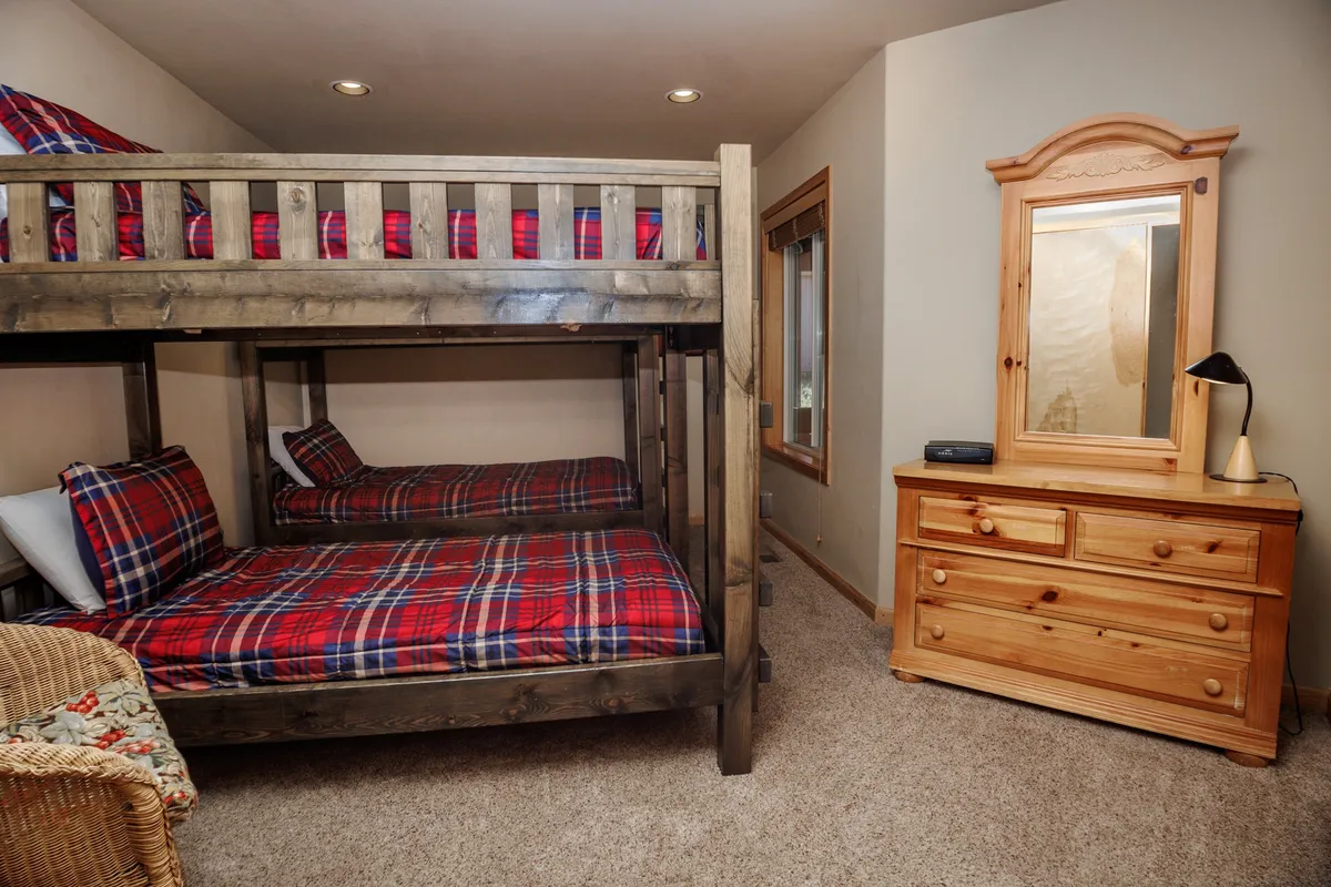 This image showcases a warm and inviting bunk room with wooden bunk beds, a wooden dresser, and plaid bedding. The space is styled for comfort and is clearly designed for children, highlighted by playful details that invite storytelling and family bonding.
