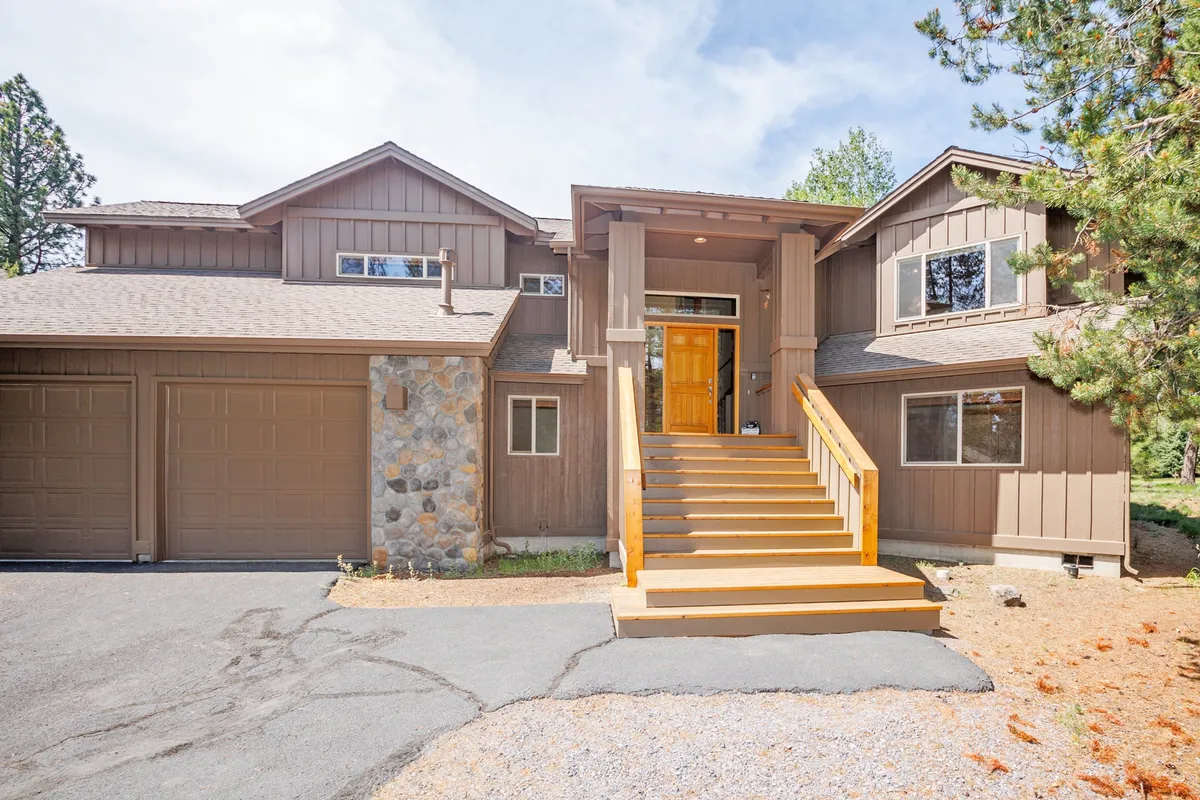 A wide exterior shot of the home's main entrance, featuring stairs, stone accents, and garage doors. The surrounding environment hints at access to neighborhood amenities, trails, and recreational opportunities just beyond the doorstep.